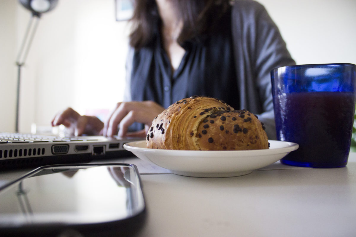 家で朝食を食べながらパソコンをする女性